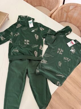 Nike kids green tracksuit with white Nike swoosh and text graphics.